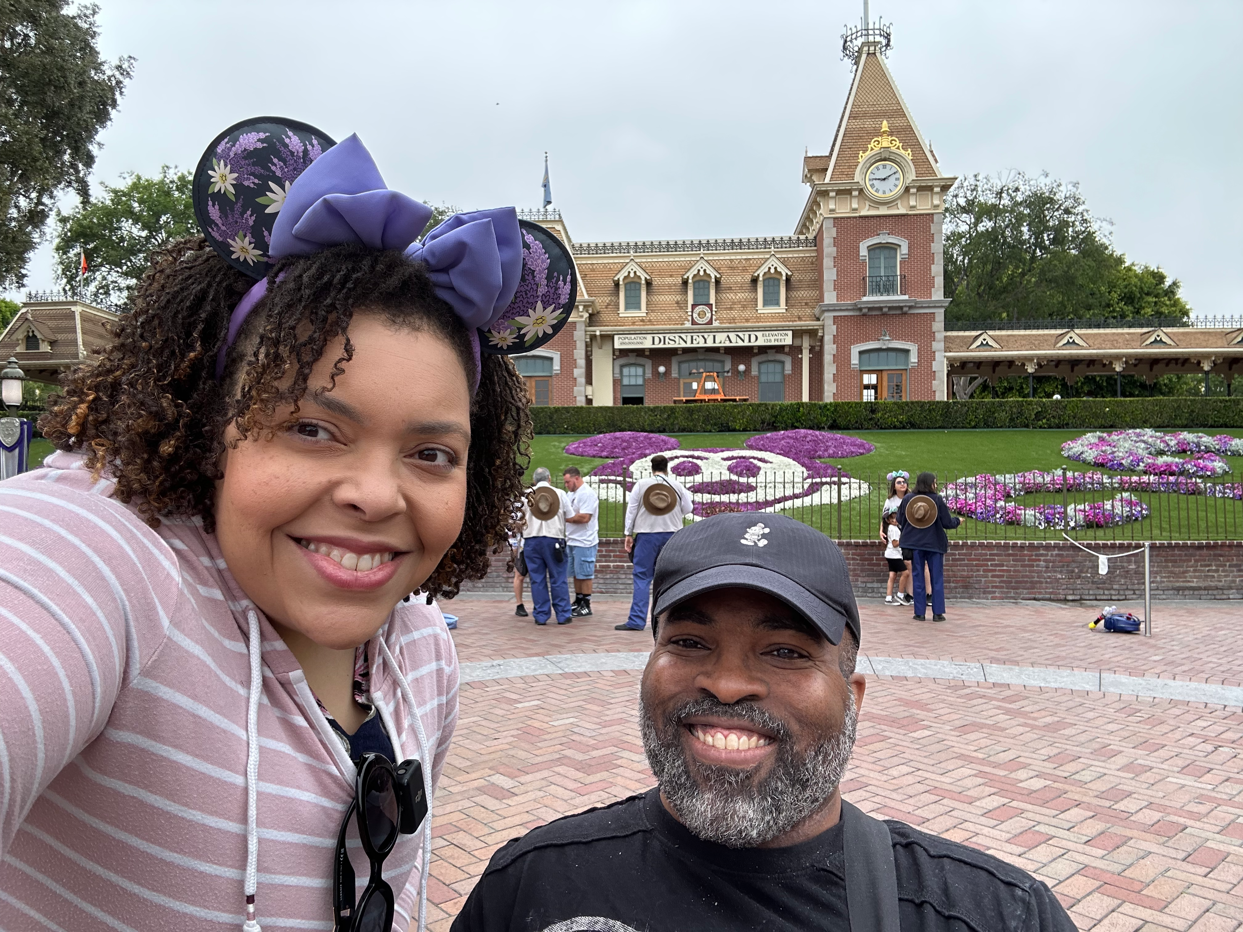 Couple stands in front of garden at the entrance to Disneyland park